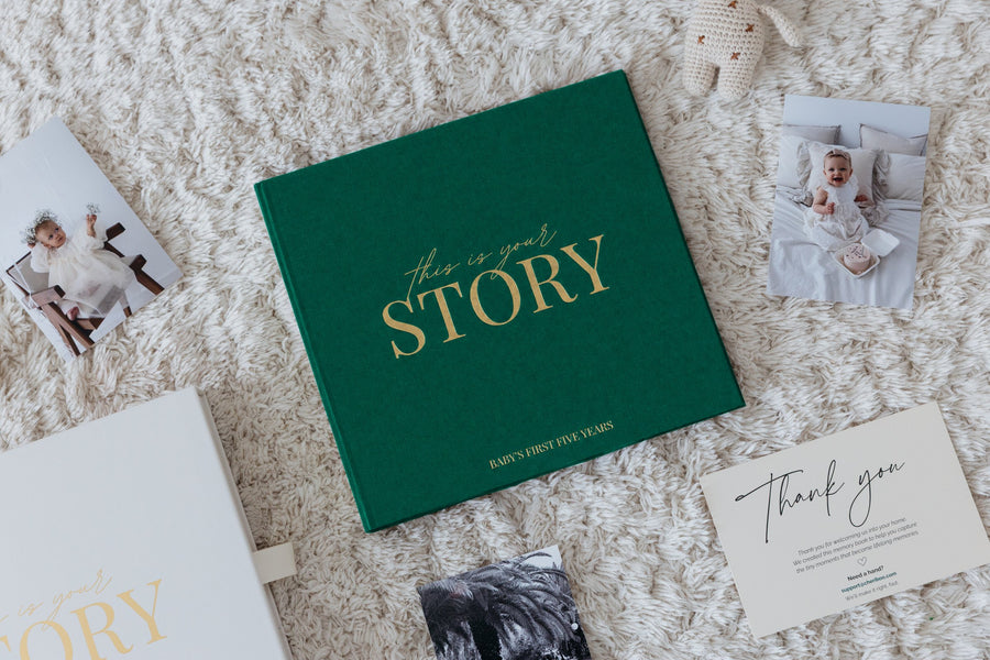 Close-up of the CheriBOO Baby Memory Book in Evergreen with its gold foil title, next to printed photos and the keepsake box