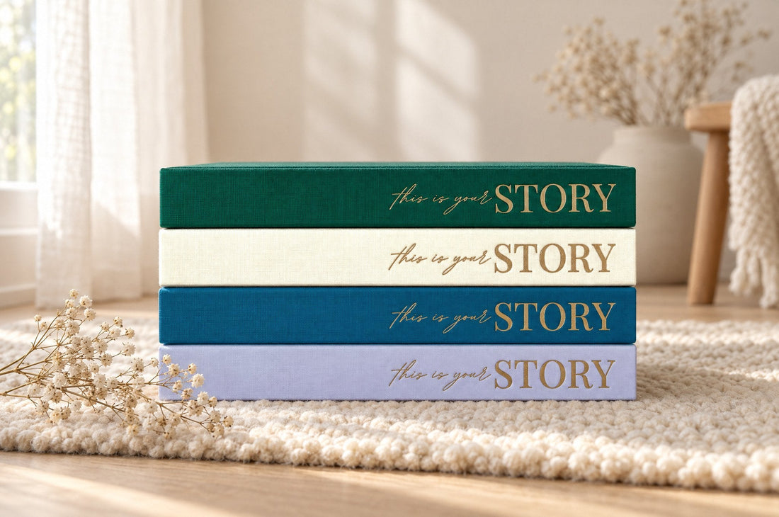 Four CheriBOO baby memory books stacked with their spines out, in Evergreen, Natural, Deep Sea Blue and Lavender