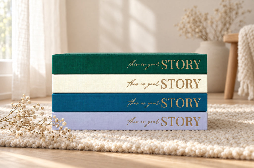 Four CheriBOO baby memory books stacked with their spines out, in Evergreen, Natural, Deep Sea Blue and Lavender