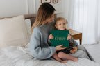 A mother and her toddler hold the CheriBOO Baby Memory Book in Evergreen, linen cover with gold foil