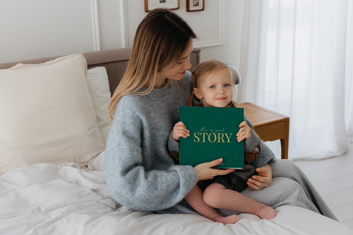 A mother and her toddler hold the CheriBOO Baby Memory Book in Evergreen, linen cover with gold foil