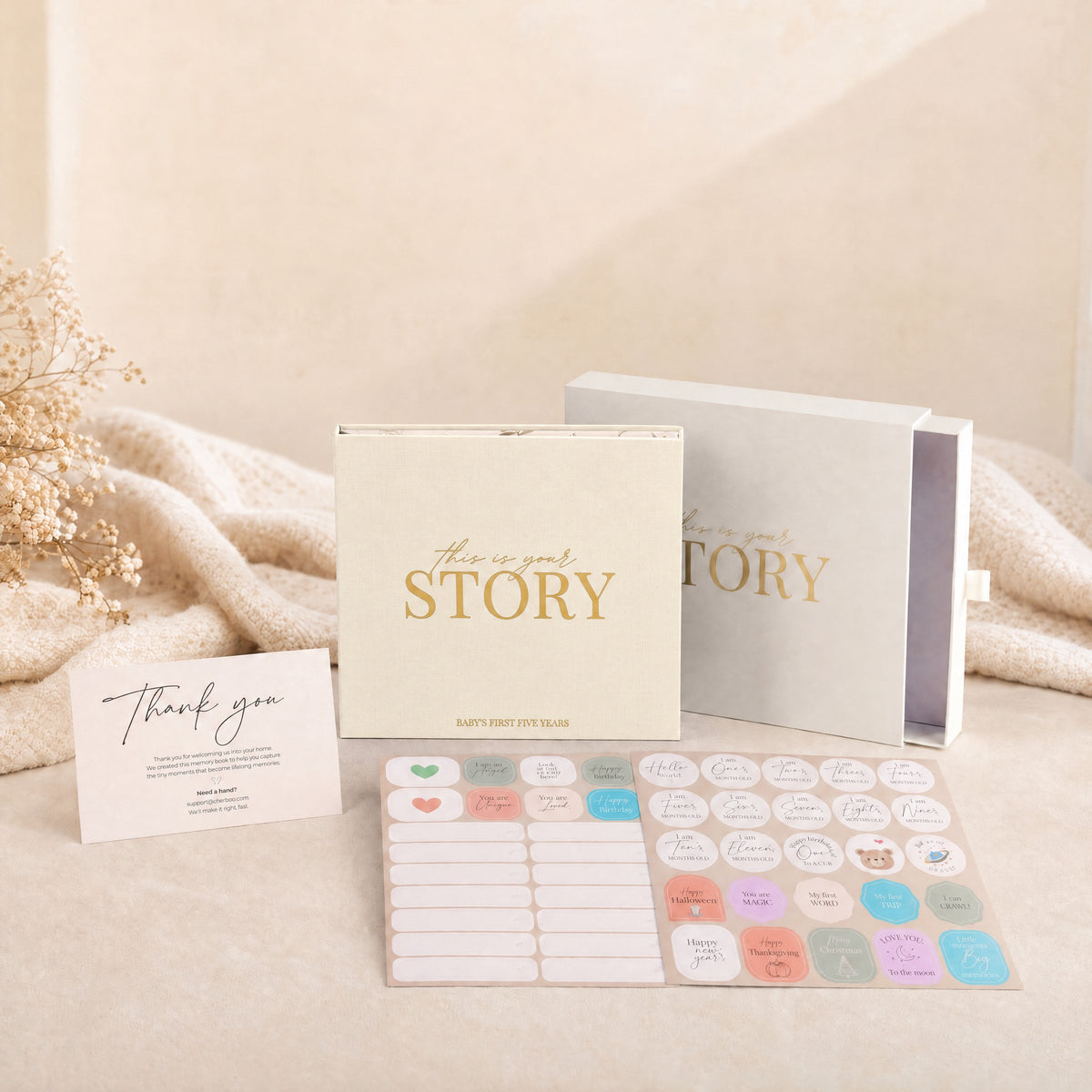 The CheriBOO Baby Memory Book in Natural with its keepsake box, thank-you card and two sticker sheets on a linen throw